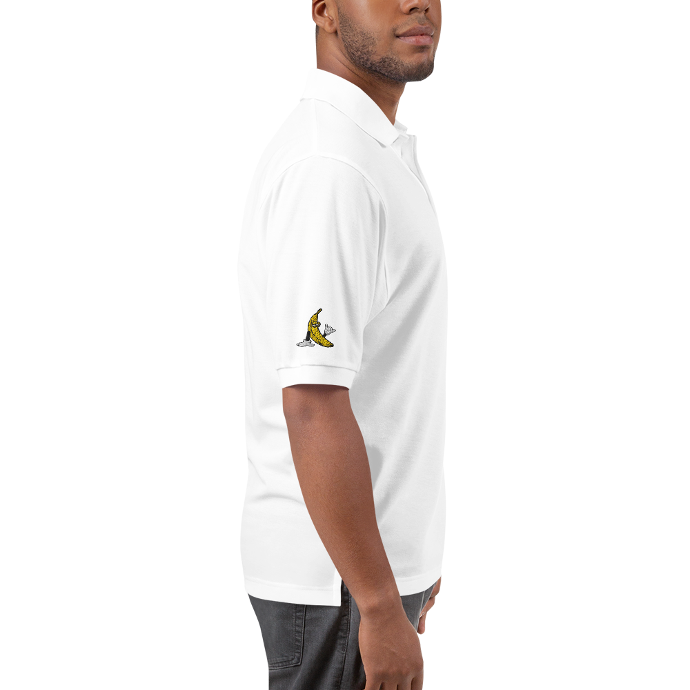 Model wearing white short sleeved, collared polo t-shirt. Model is in profile view, an embroidered logo of the cartoon banana holding up a shaka is on the right sleeve.