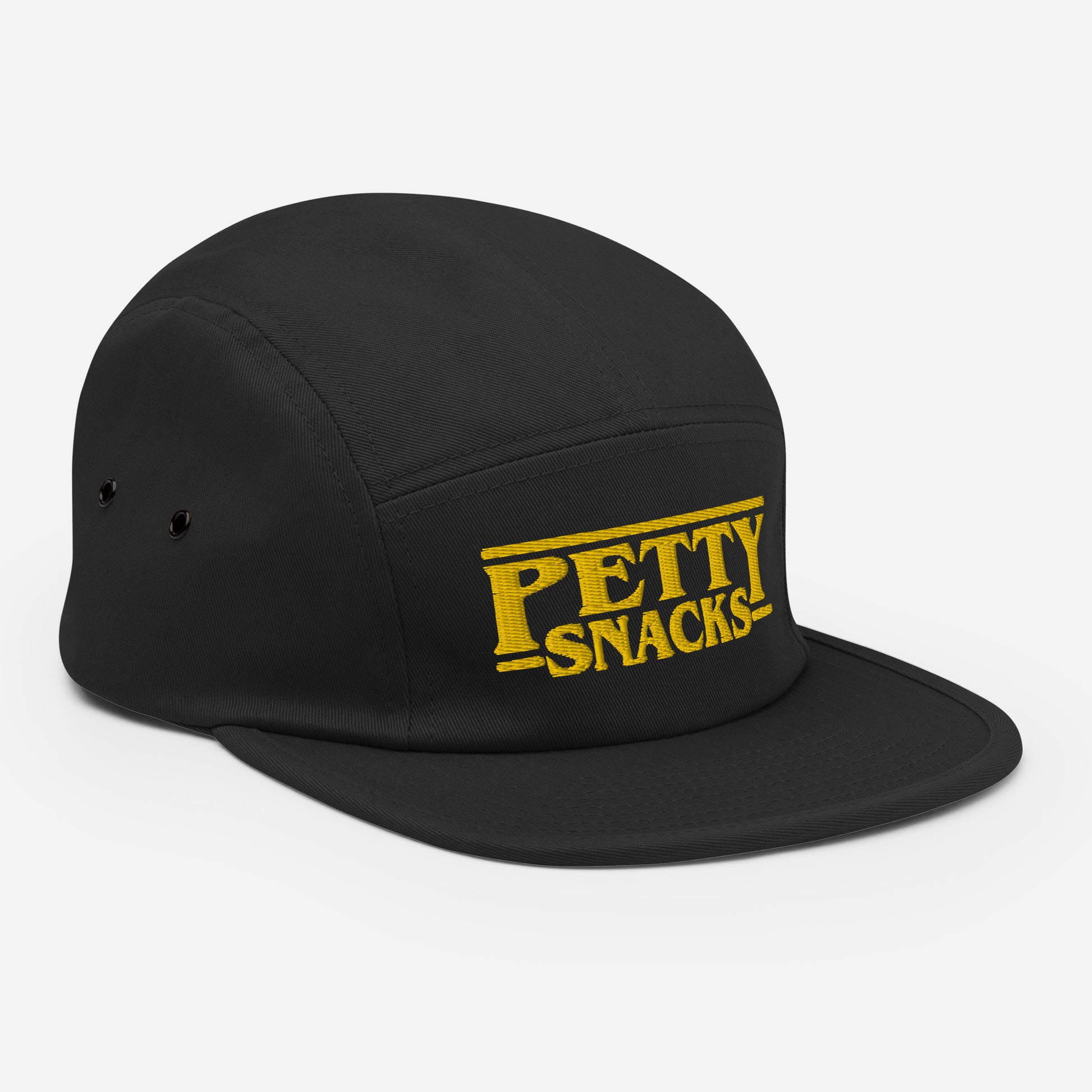 Side view of a black five-panel hat with embroidered lettering in front center. Letterings says "Petty Snacks" in yellow with a line on top and bottom of the words. In the style of film credits made famous by Tarantino.